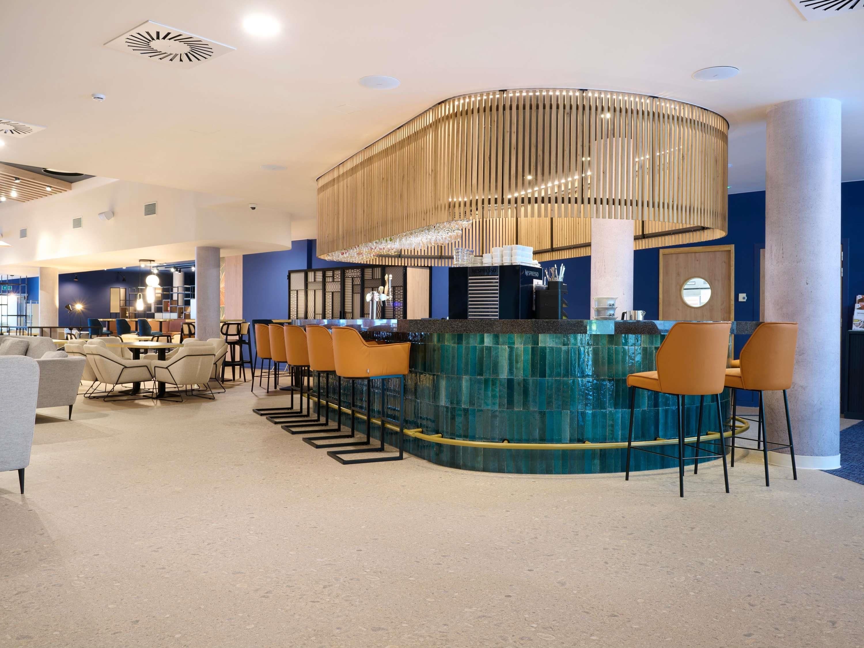 Un espace bar moderne doté d’un comptoir incurvé, de tabourets de bar et d’un luminaire décoratif.