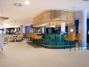 Zona de bar moderna con una barra curva, taburetes y una lámpara decorativa.