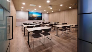 A conference room with a large screen, multiple tables, and chairs.