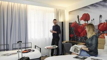 Habitación de hotel con dos camas, una mesita pequeña y un ventanal con cortinas traslúcidas.