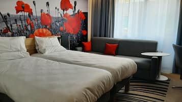 A hotel room with two beds, a grey sofa, a small round table, and a large window with curtains.