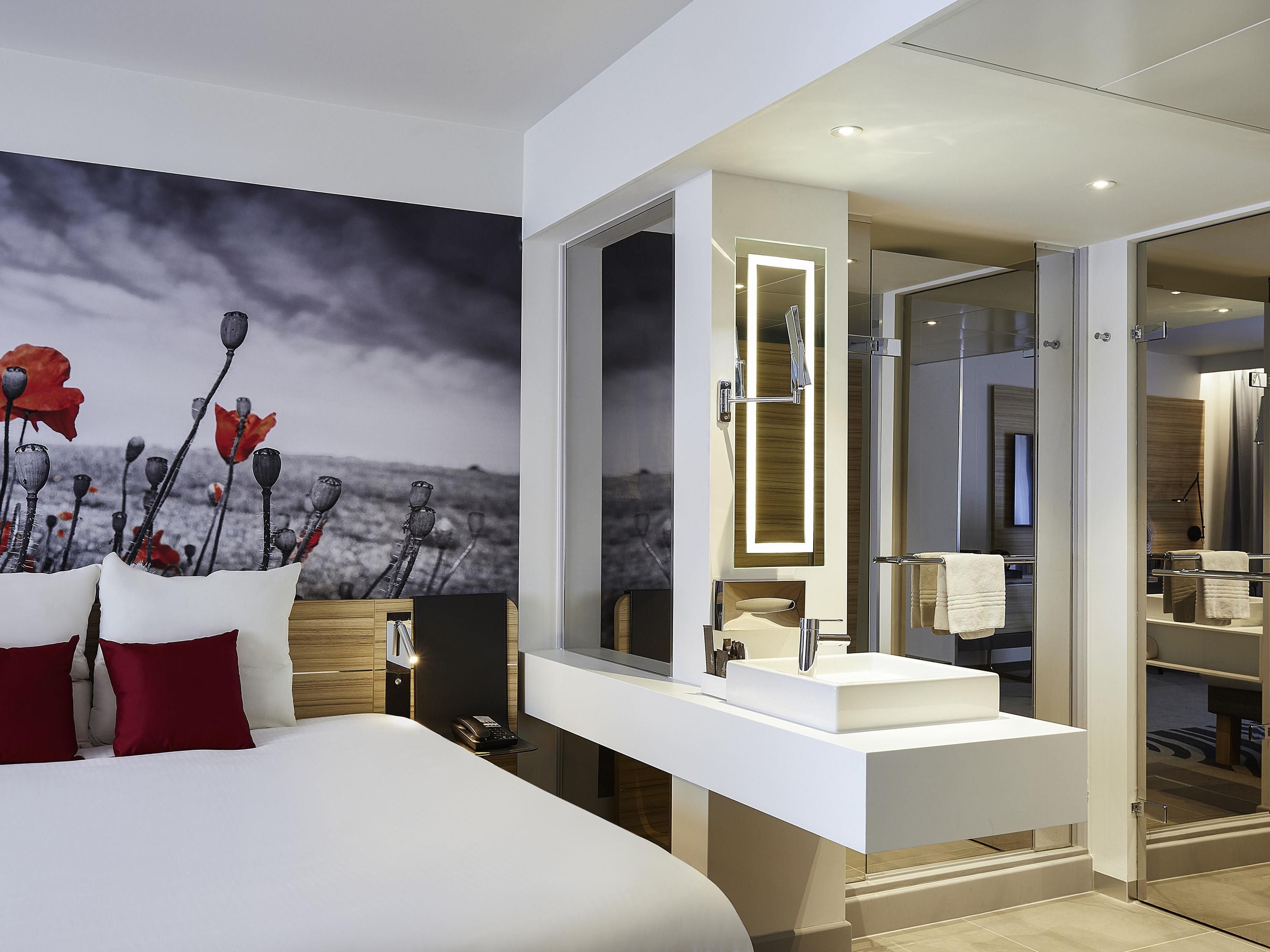Een moderne hotelkamer met een groot bed, een witte kaptafel met spiegel en uitzicht op zee.
