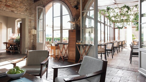 A spacious indoor area with arched windows, wooden furniture, and hanging plants. - Relais Villa Olmo (Impruneta)