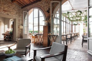A spacious indoor area with arched windows, wooden furniture, and hanging plants. - Relais Villa Olmo (Impruneta)