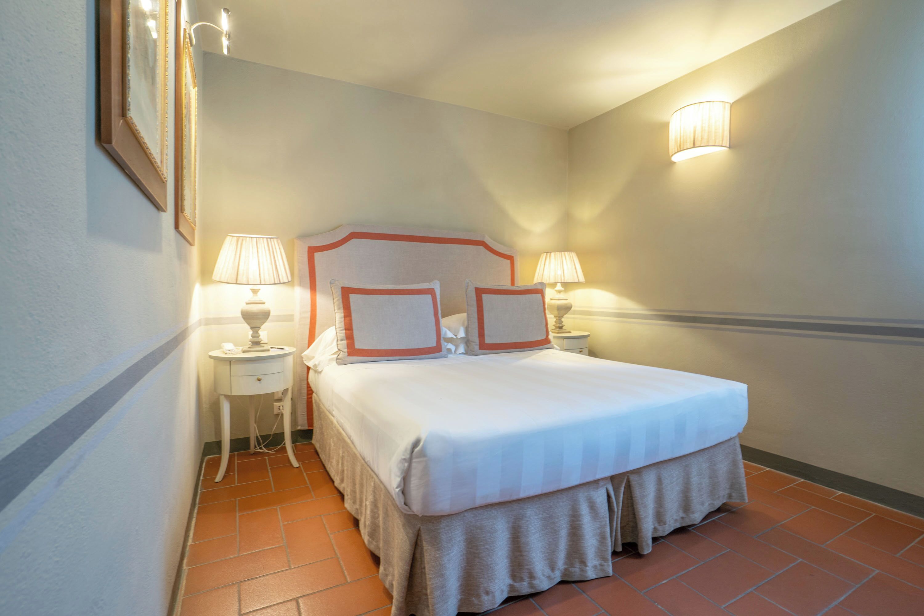 Une chambre d’hôtel comprenant un lit, deux tables de chevet, deux lampes, une tête de lit et un luminaire fixé au mur.