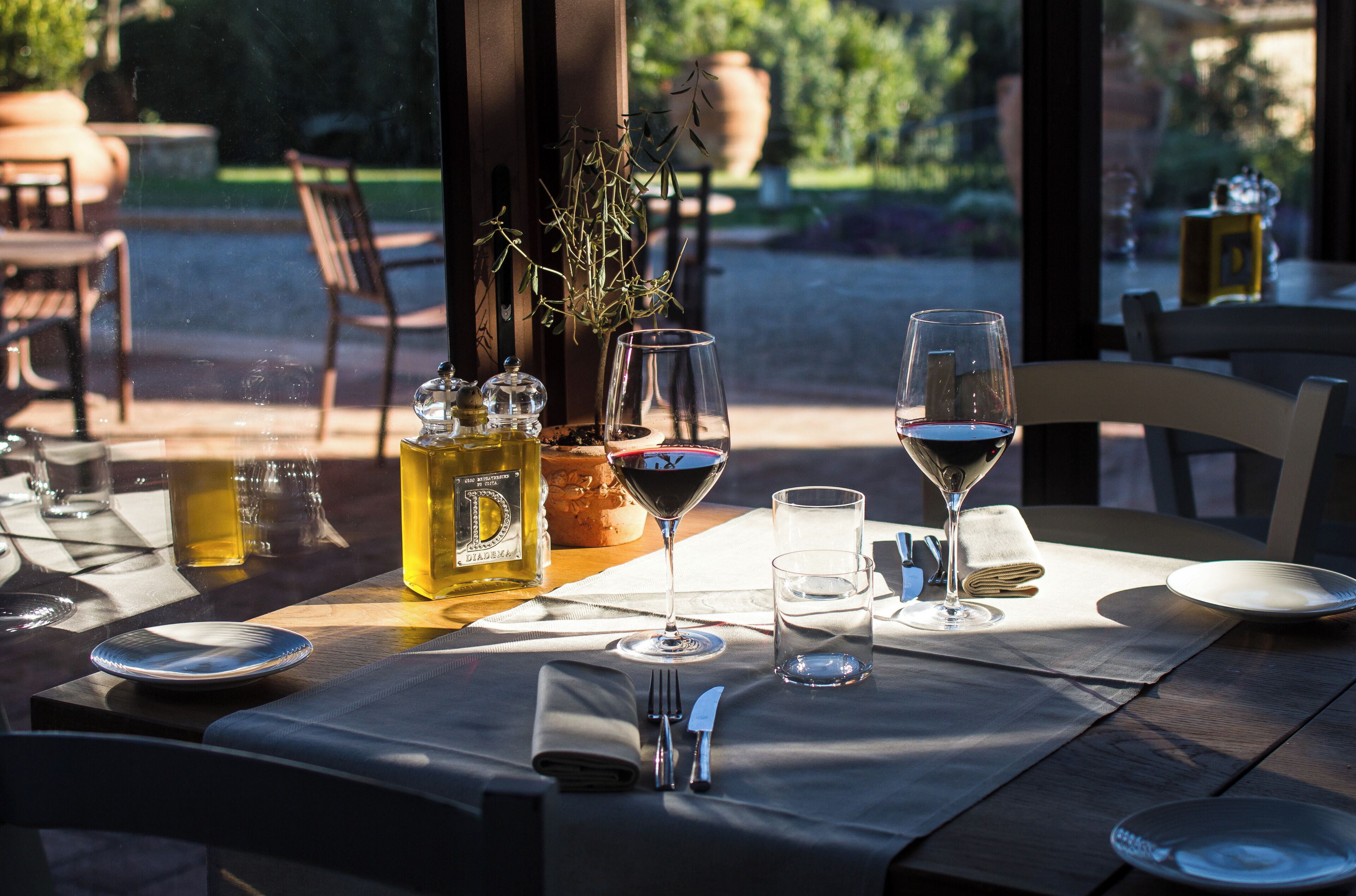An outdoor dining table set with wine glasses, a bottle of olive oil, and a potted plant.