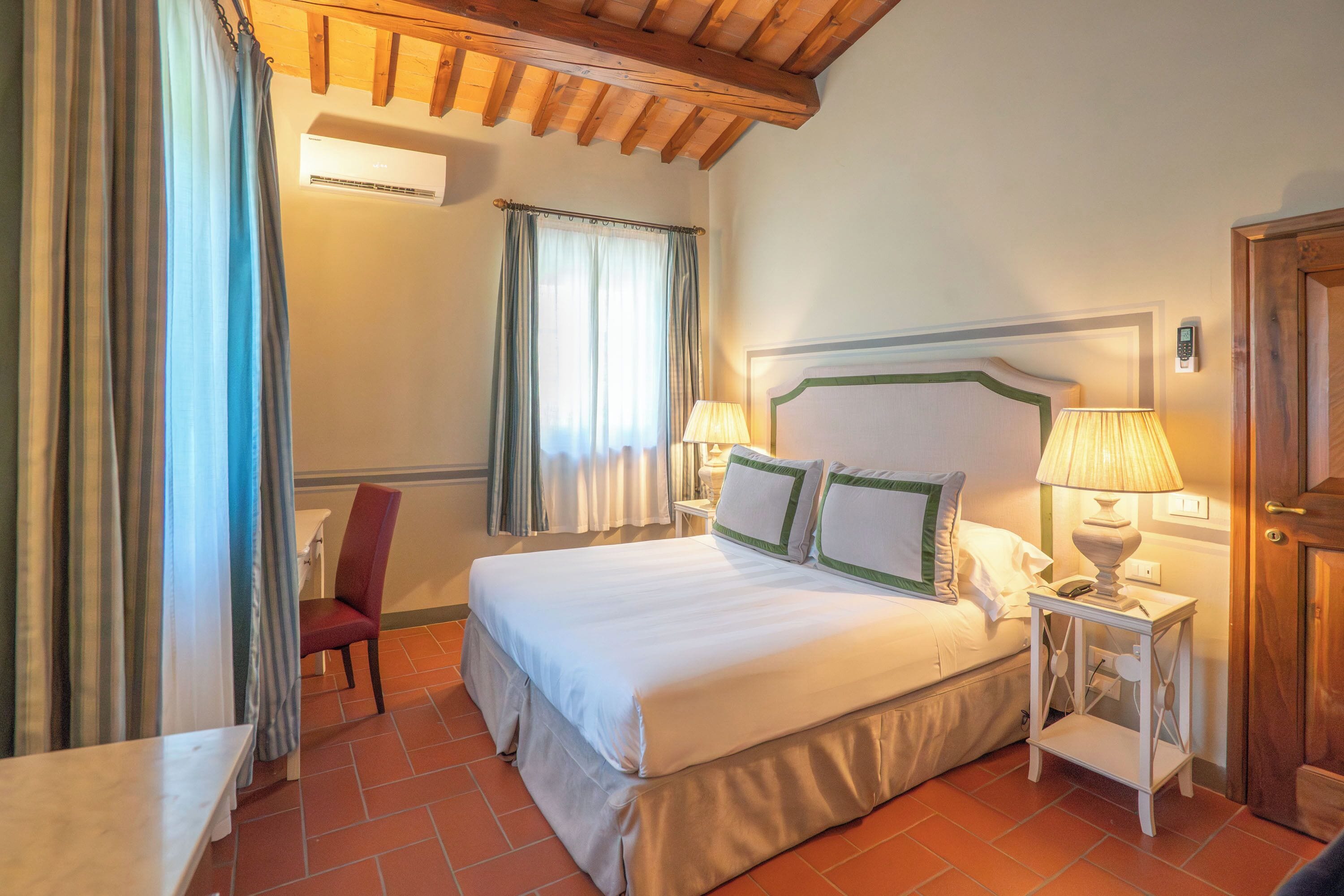 A hotel room with a bed, bedside table, lamp, chair, and curtains.