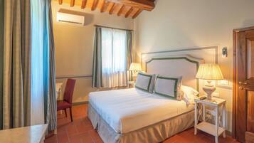 A hotel room with a bed, bedside table, lamp, chair, and curtains.