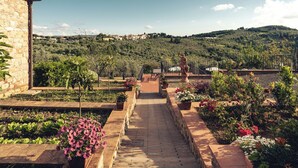 A stone pathway leading to a terrace with potted plants and flowers, overlooking a hillside with houses. - Relais Villa Olmo (Impruneta)