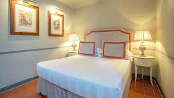 A neatly made bed with white linens and a grey skirt, two bedside lamps, and two framed pictures on the wall.