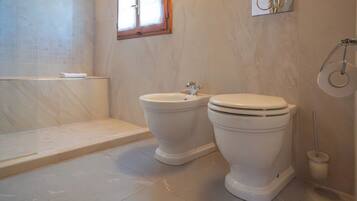 Une salle de bain avec deux toilettes, un bidet, une fenêtre et un porte-rouleau de papier toilette.
