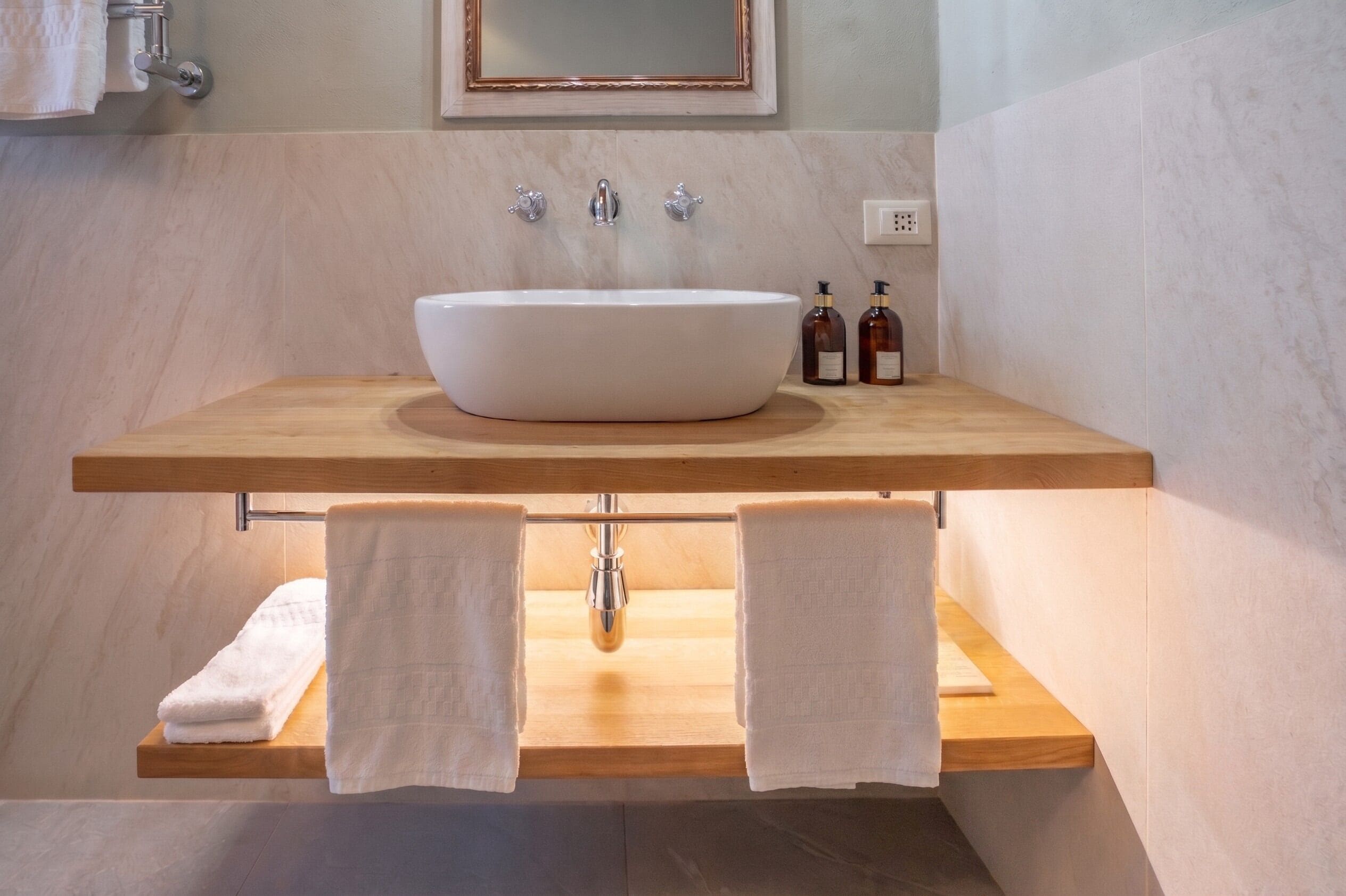 A bathroom with a large vessel sink, wooden countertop, two towel racks, and a mirror above the sink.