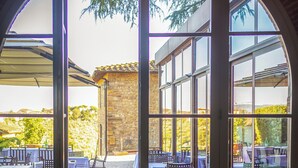 An outdoor dining area with tables set for a meal, large windows, and a stone wall in the background. - Relais Villa Olmo (Impruneta)