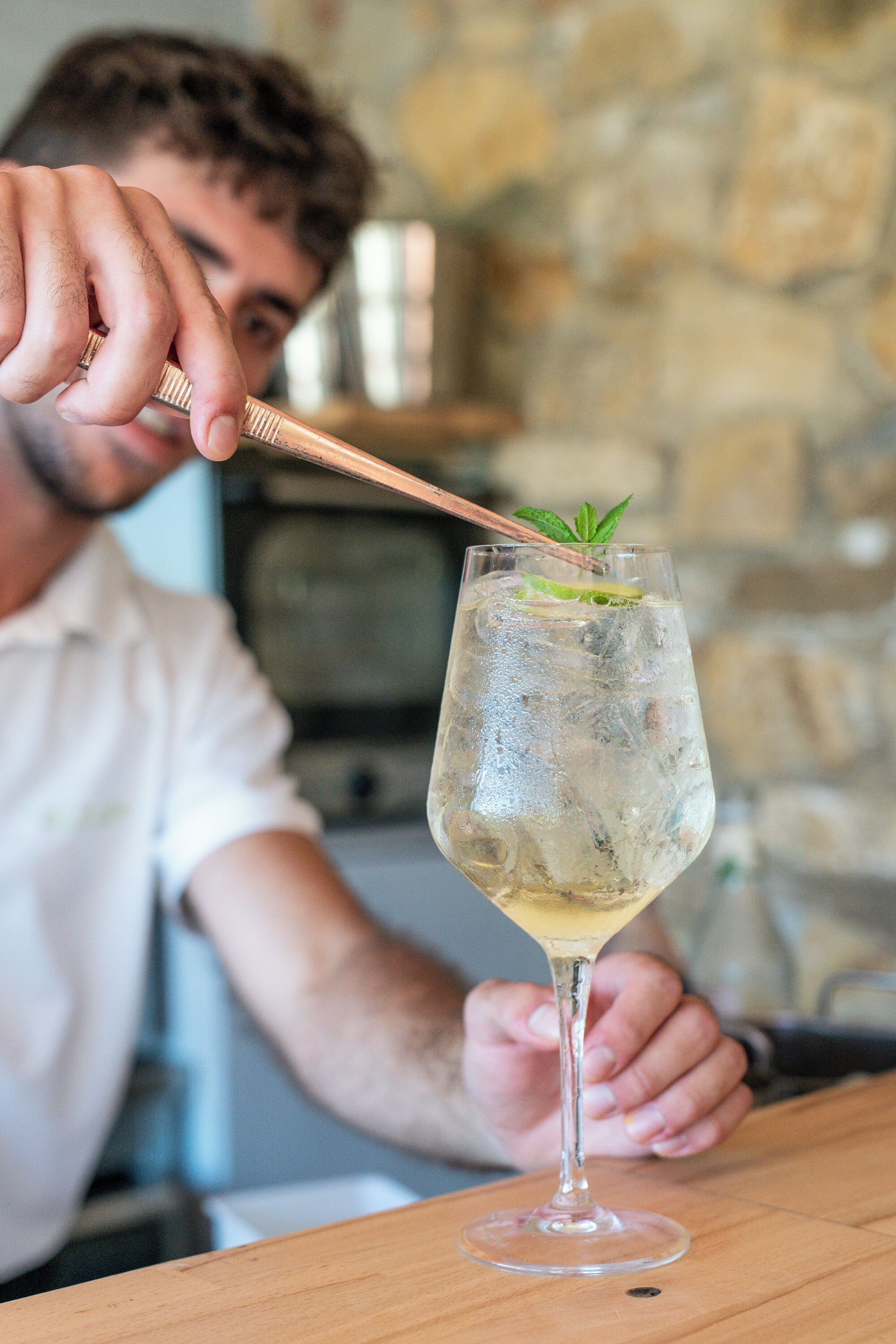 A person holding a cocktail glass with ice and mint garnish.