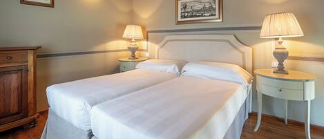 A double bed with white linens, two bedside tables with lamps, a wooden wardrobe, and two framed pictures on the wall.