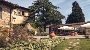 A stone building with a garden, outdoor seating, and a large tree. - Relais Villa Olmo (Impruneta)