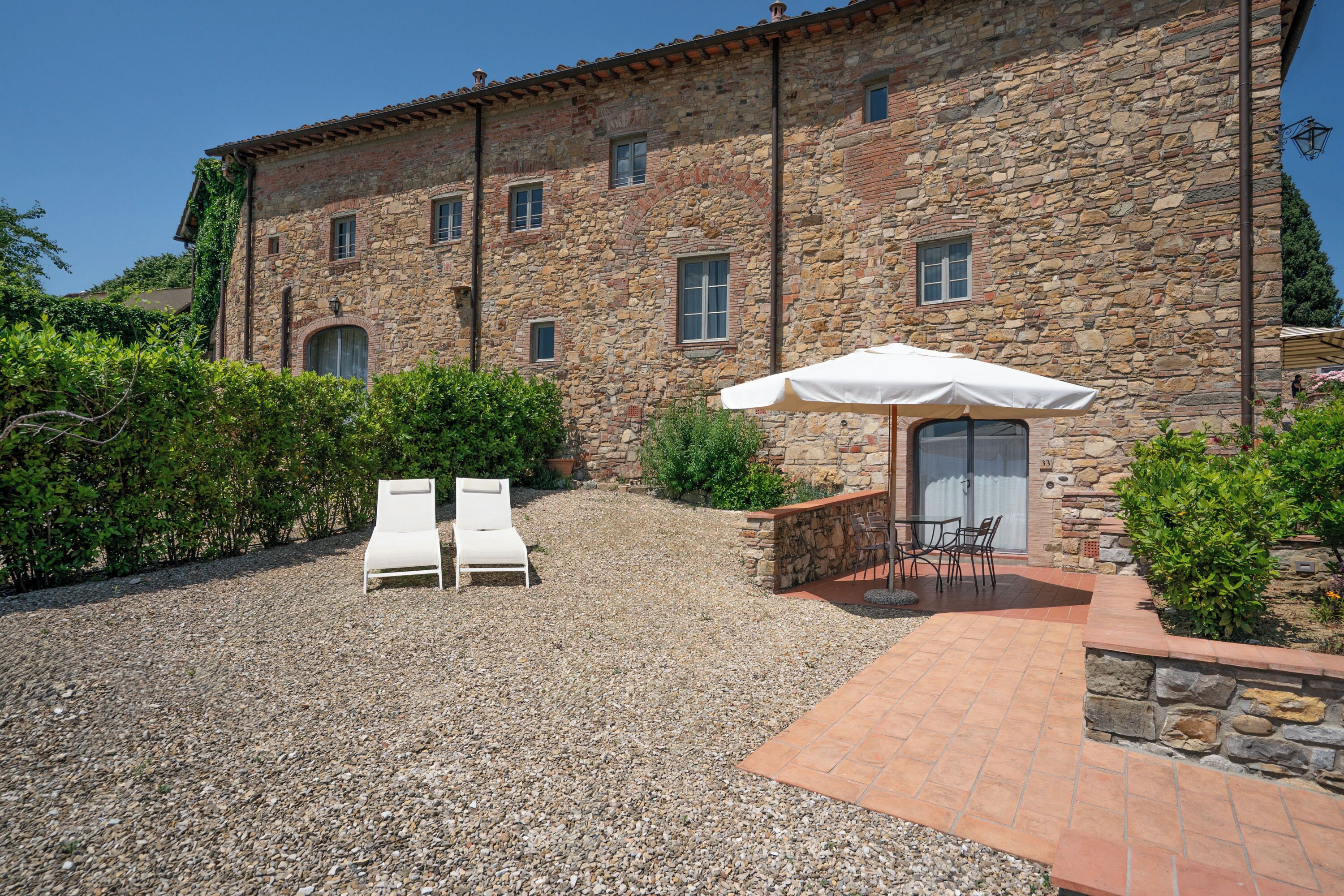 A stone building with a patio area featuring two lounge chairs and a table with an umbrella.