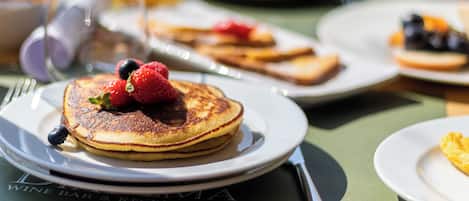 Un desayuno con tortitas, fresas y arándanos en un plato.