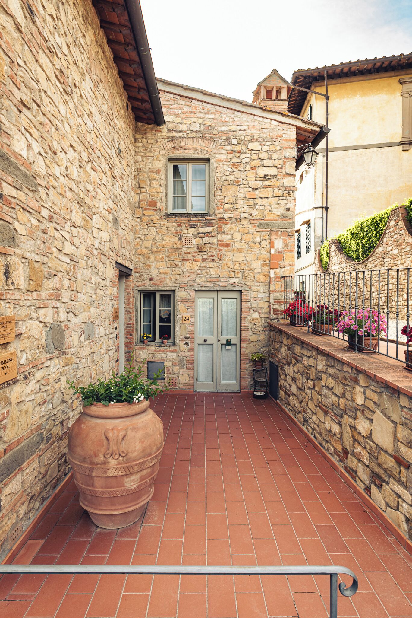 Un edificio de piedra con un patio adoquinado, una jardinera grande y una barandilla de metal con flores.
