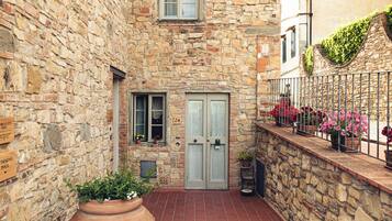 Un edificio de piedra con un patio adoquinado, una jardinera grande y una barandilla de metal con flores.