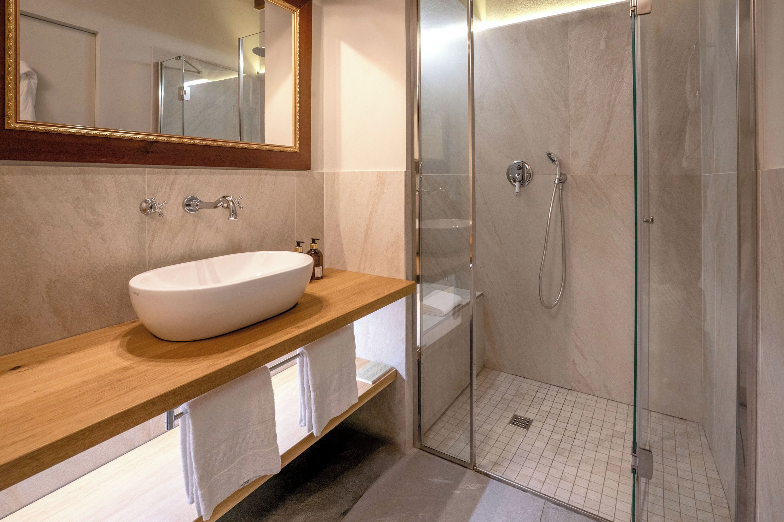 A modern bathroom with a large white sink, a glass shower enclosure, and a wooden vanity.