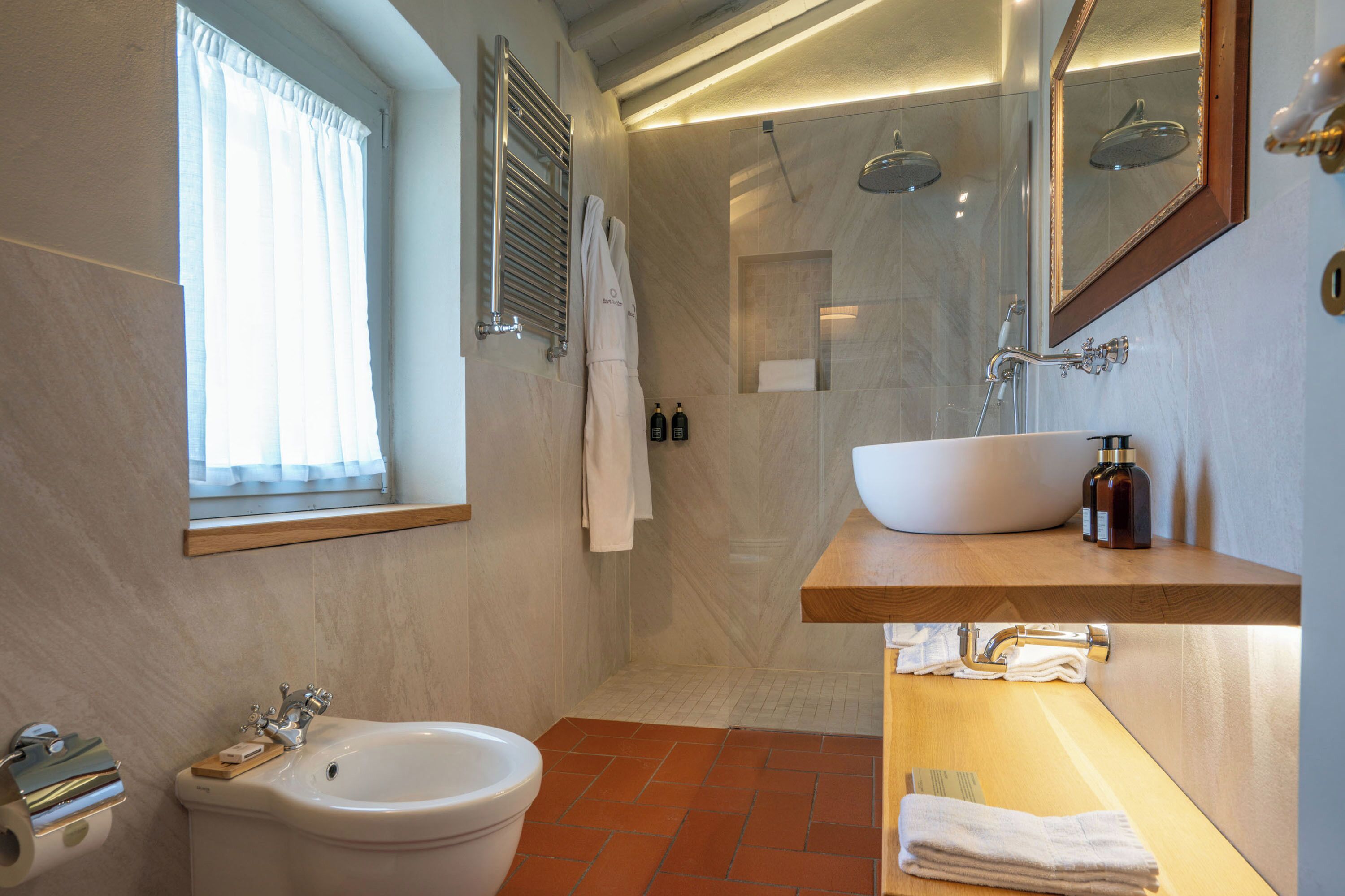 A bathroom with a bidet, a sink, a mirror, and a shower.