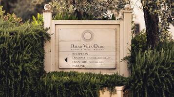 A sign for Relais Villa Olmo, a food and wine resort, with directions to Reception, Diadema Wine Bar & Restaurant, Frantoio Olive Oil Mill, and Parking.