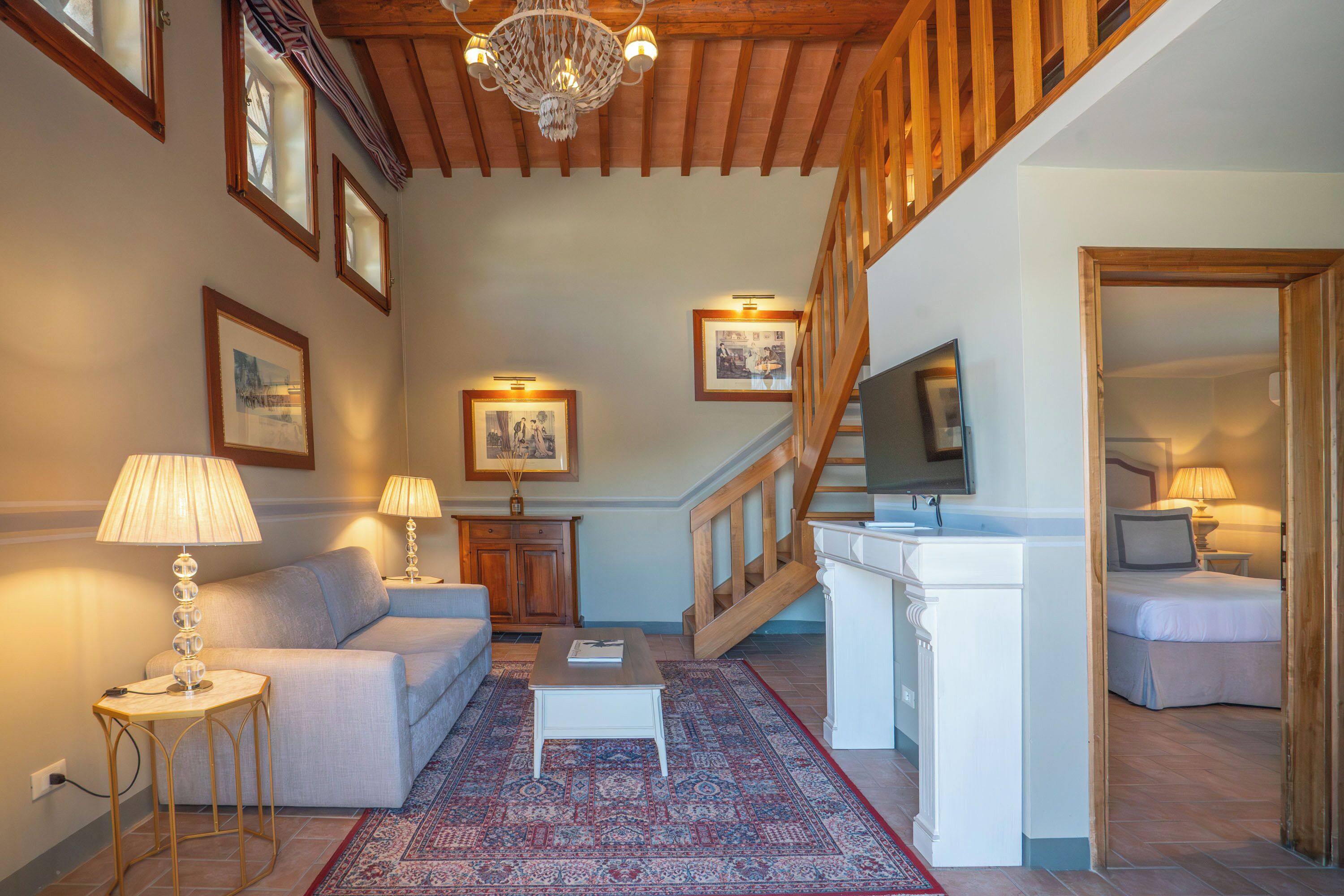 Un soggiorno con divano, tavolino, tappeto decorato, scala in legno e televisione.