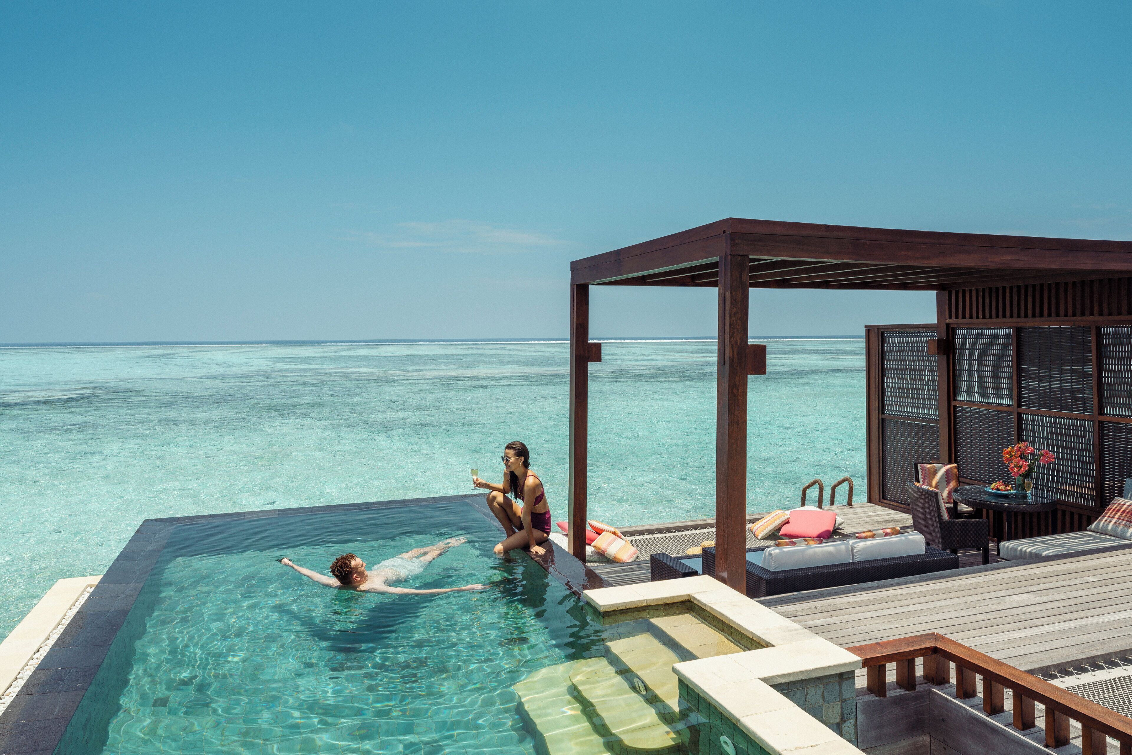 A poolside area with a wooden deck, lounge chairs, and a view of the ocean.