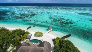 Vista aérea de un resort tropical con un mar turquesa cristalino, una playa arenosa y construcciones de techo de paja.