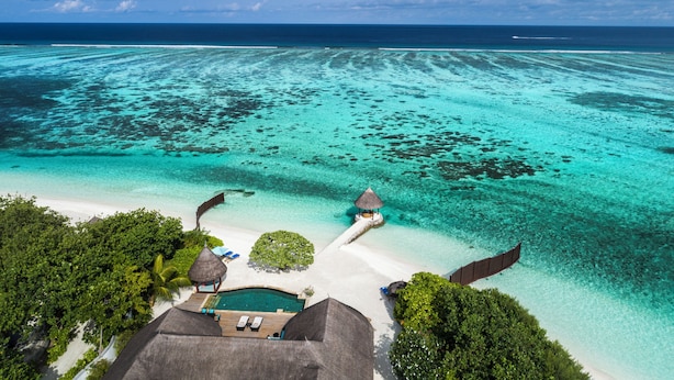 Ein Luftbild eines tropischen Resorts mit klarem türkisblauem Meer, einem Sandstrand und strohgedeckten Gebäuden.