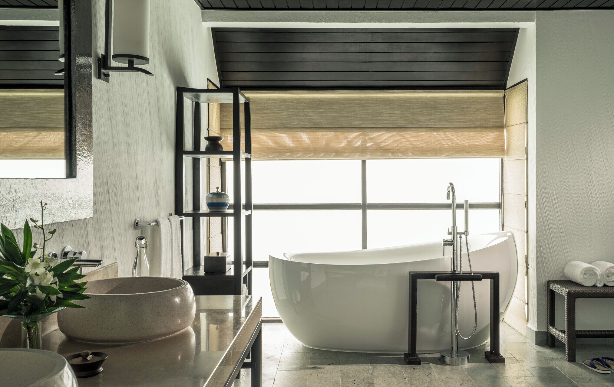 A modern bathroom with a freestanding bathtub, a large mirror, and a window with a view.