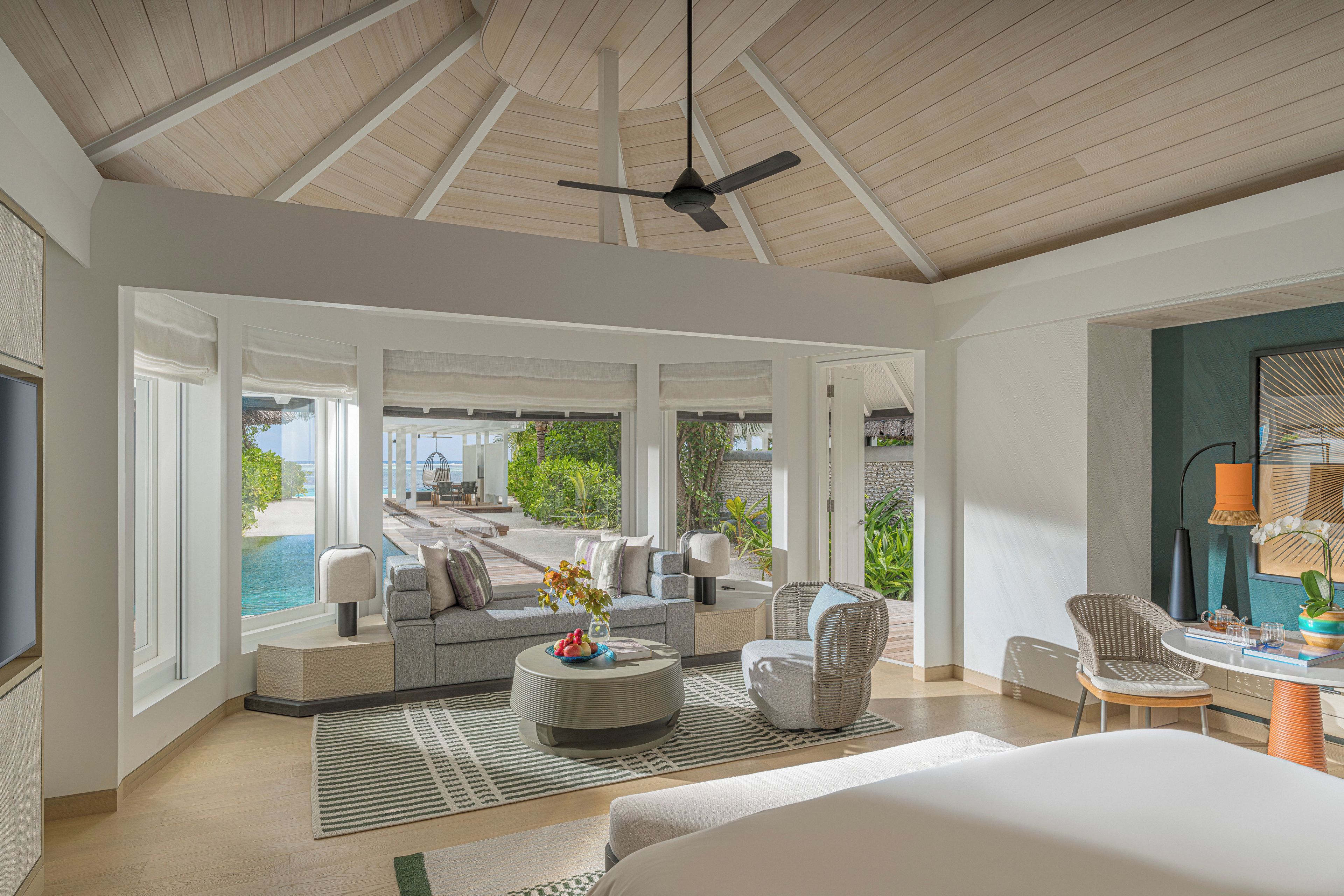 A spacious room with a large bed, a seating area with a sofa and chairs, a dining table, and a view of a pool and greenery.