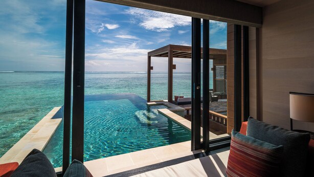 Una habitación lujosa con un amplio ventanal que da a un mar azul cristalino e una piscina infinita privada.