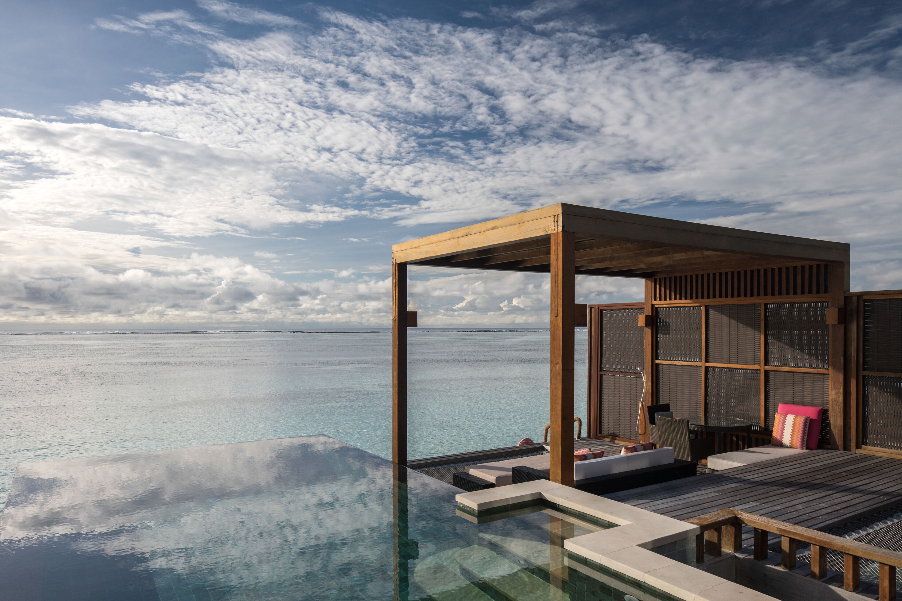 An infinity pool with a wooden deck and lounge area overlooking the ocean.
