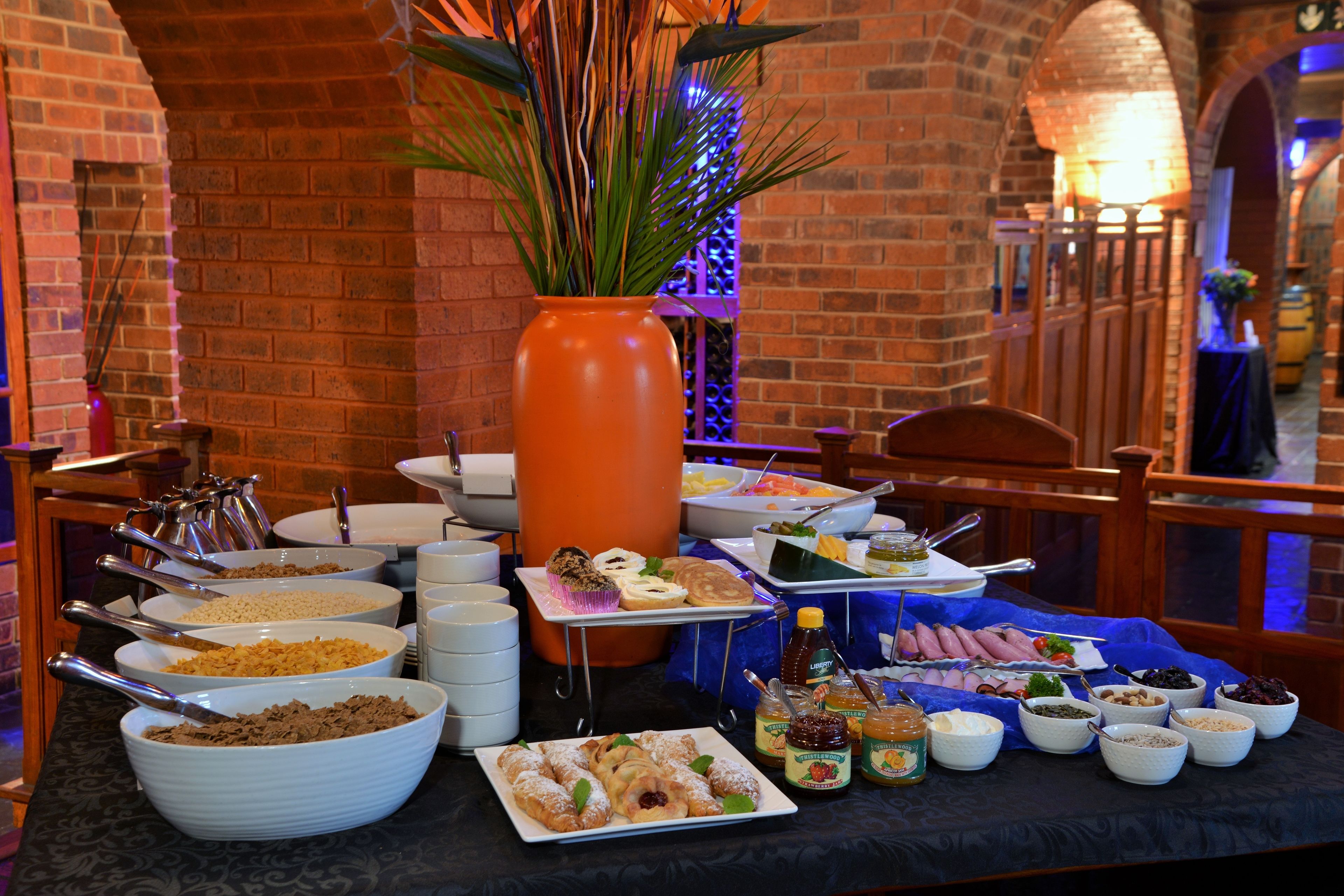 A buffet table with various food items and a large orange vase with green plants.