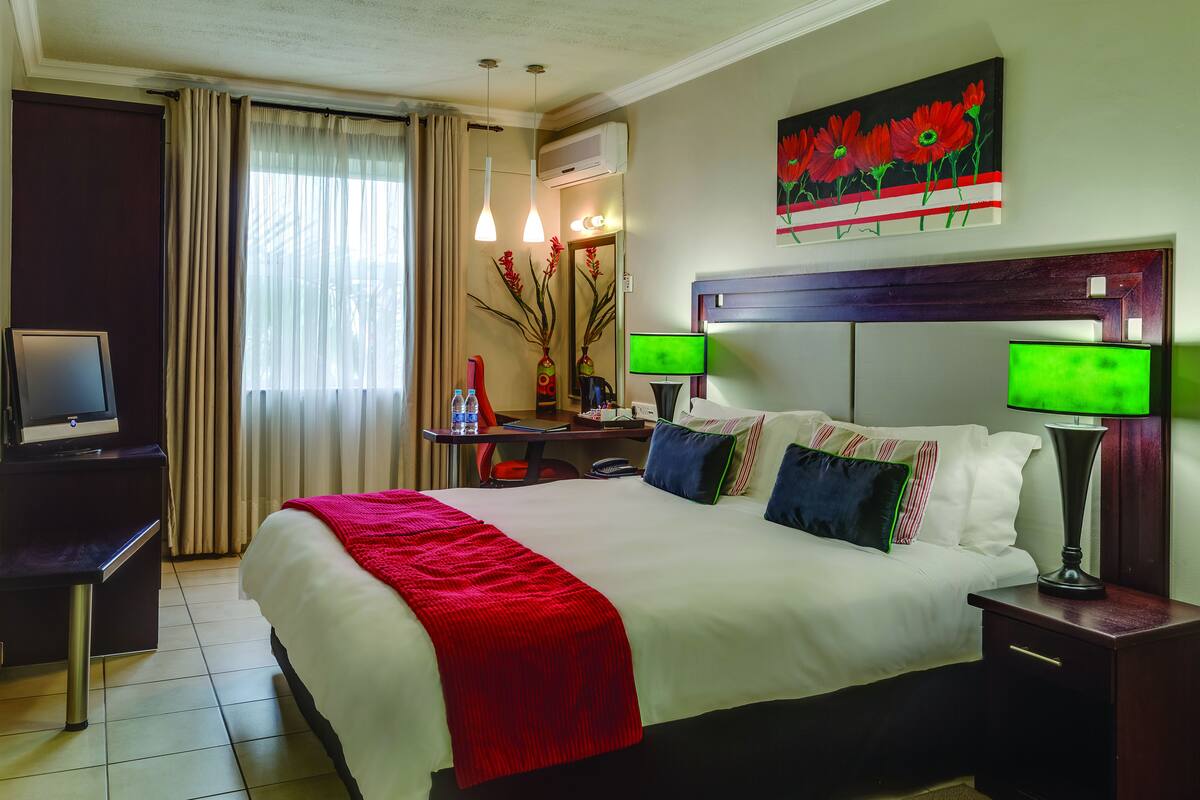 A hotel room with a large bed, two bedside tables, a desk with a chair, a TV, and a painting on the wall.