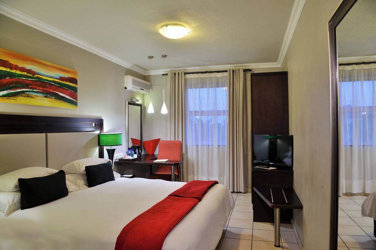 A hotel room with a bed, desk, chair, television, and a painting on the wall.