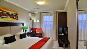 Une chambre d’hôtel avec un lit, un bureau avec une télévision, une chaise et un tableau au mur.