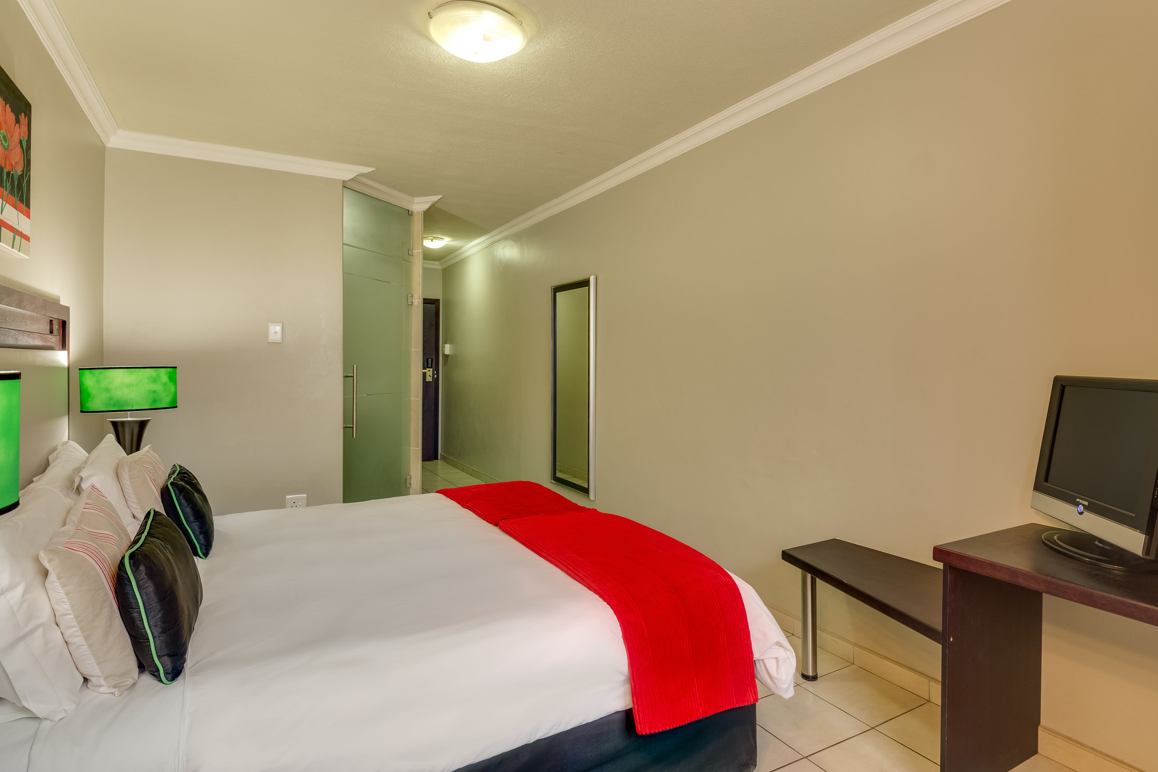 A hotel room with a bed, a desk, a television, and a mirror.