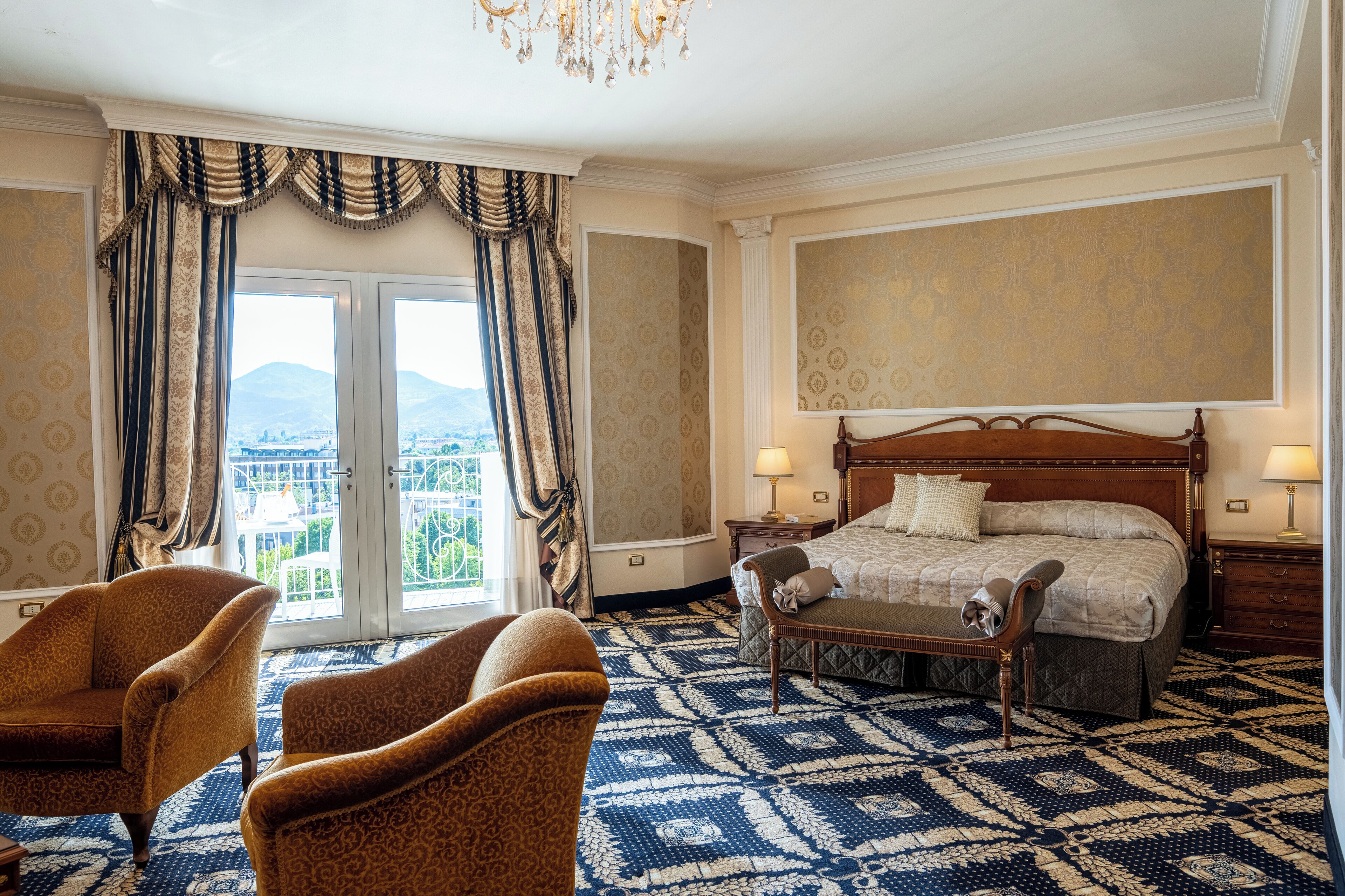 Une chambre d’hôtel avec un grand lit, deux tables de chevet, une chaise et une vue sur l’extérieur grâce à une grande fenêtre.
