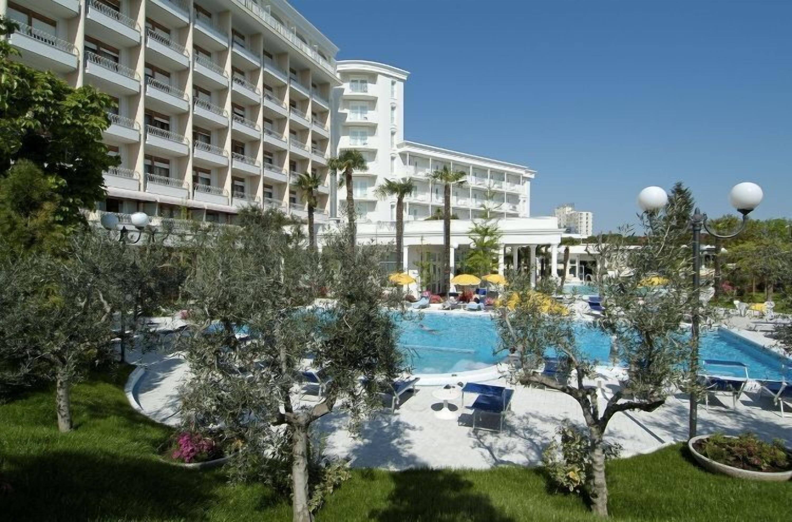 Hotel met zwembad, omringd door palmbomen en ligbedden.