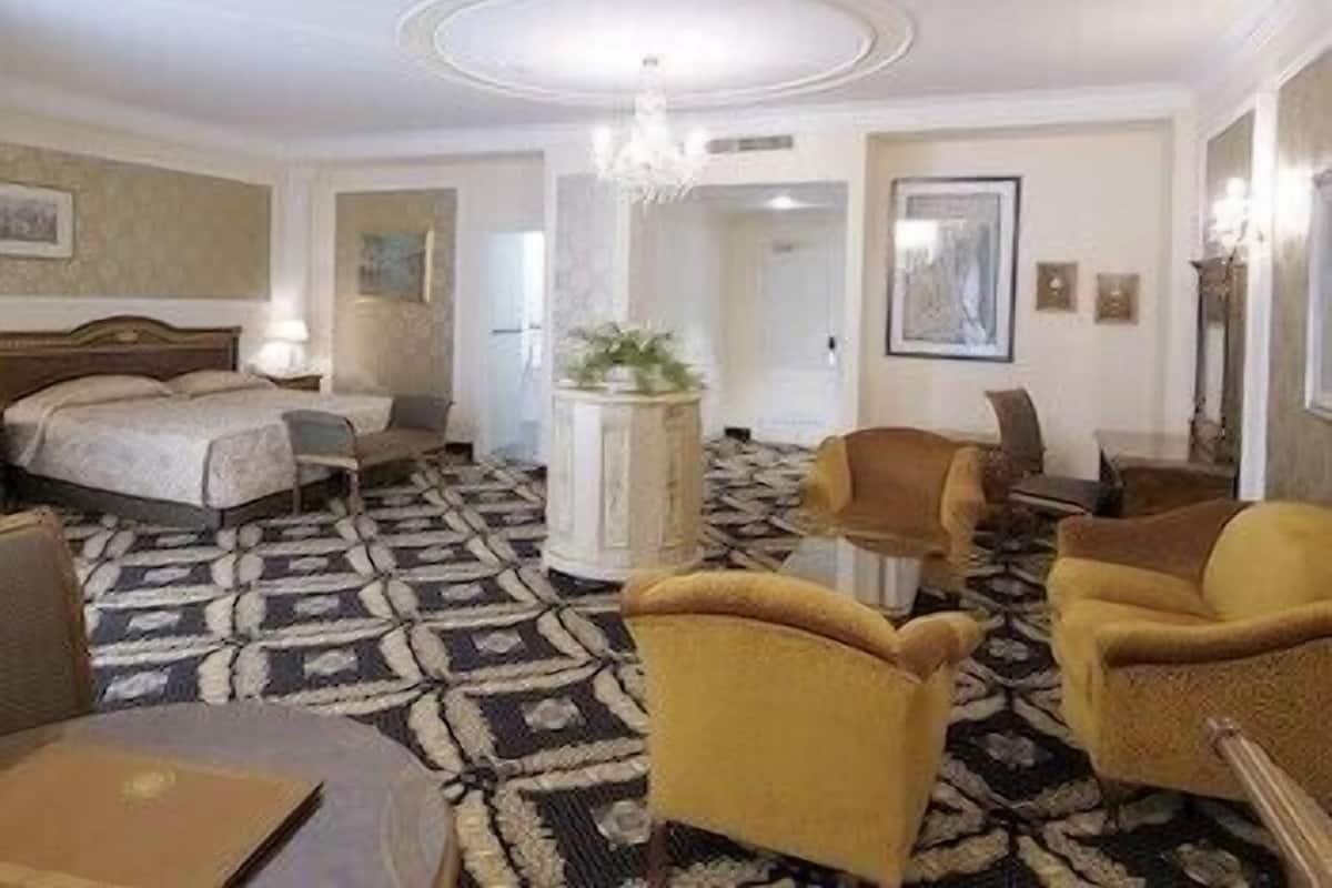 Habitación de hotel con una cama, un escritorio, dos sillones, una mesa de centro y una alfombra estampada.