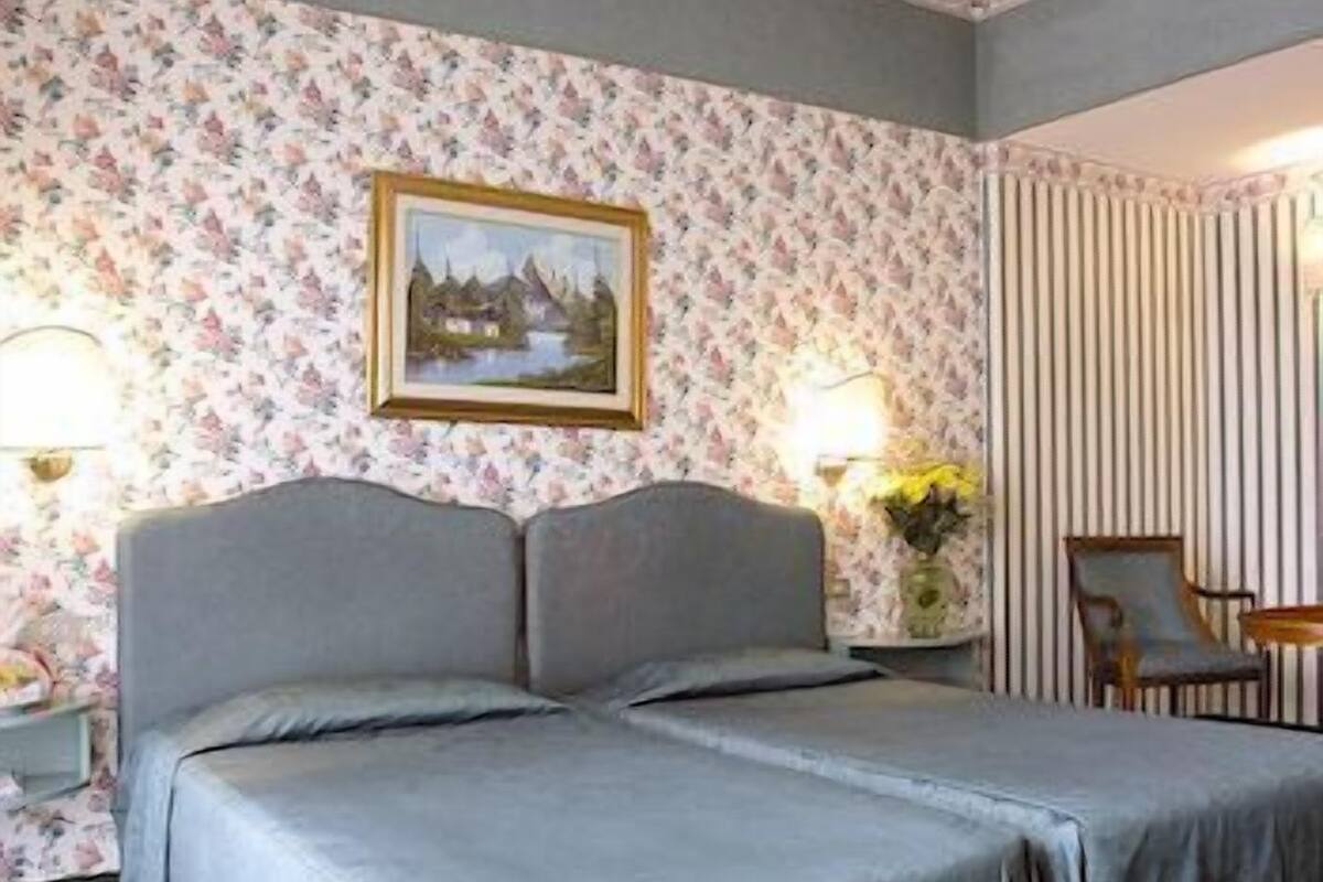 Una habitación de hotel con cama doble, papel tapiz floral, un cuadro en la pared y una cortina a rayas.