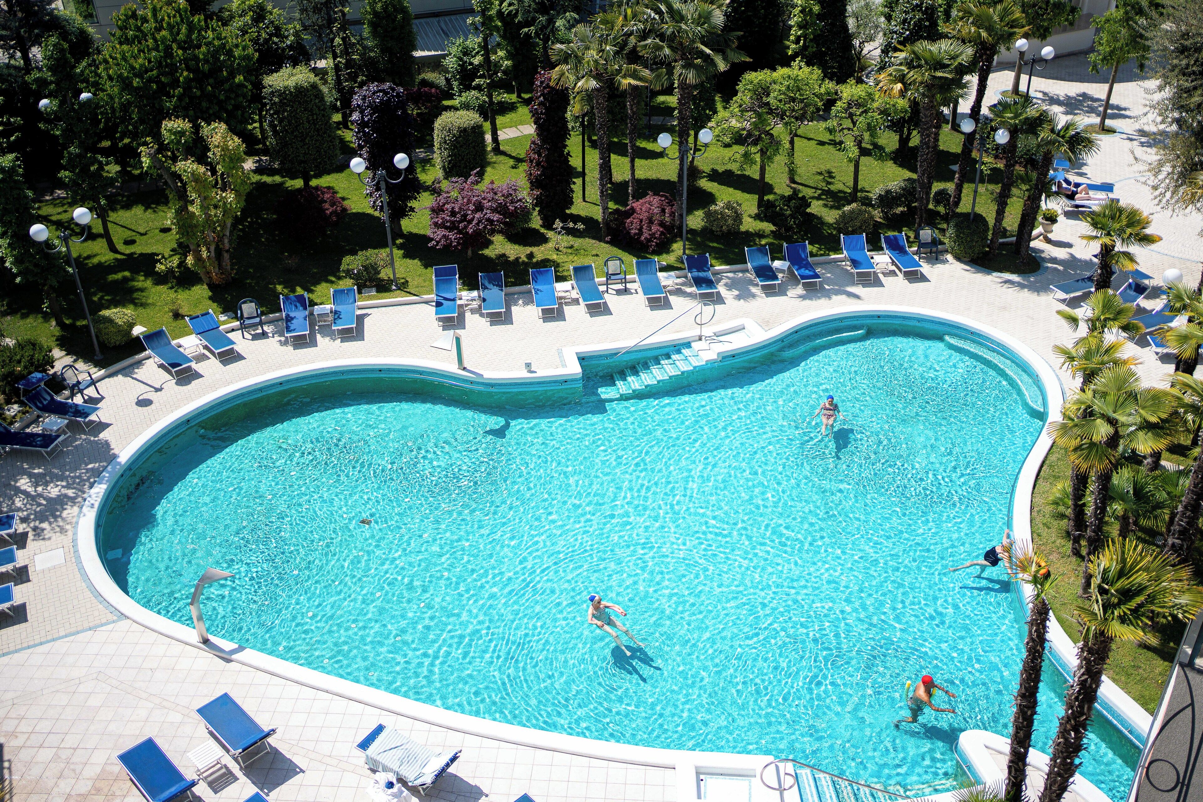 A large, curved swimming pool surrounded by lounge chairs and palm trees.