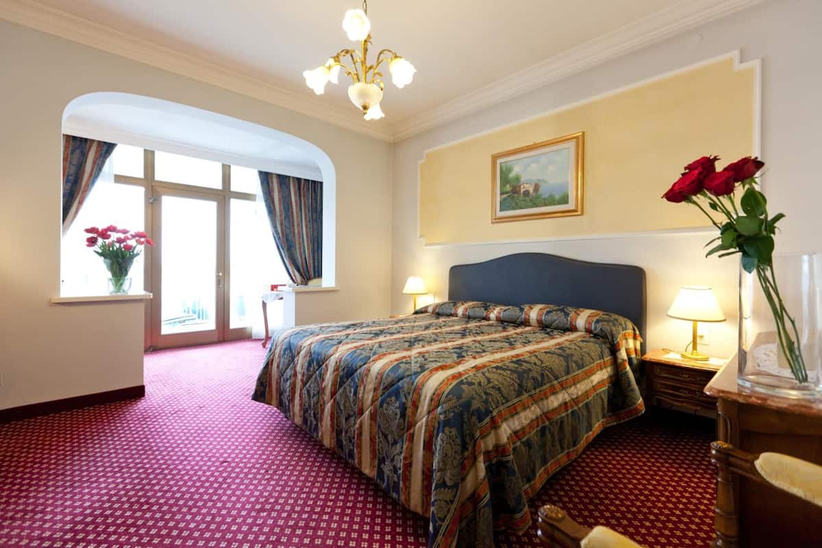 Una habitación de hotel con una cama grande, un candelabro, un cuadro en la pared y un florero con flores.
