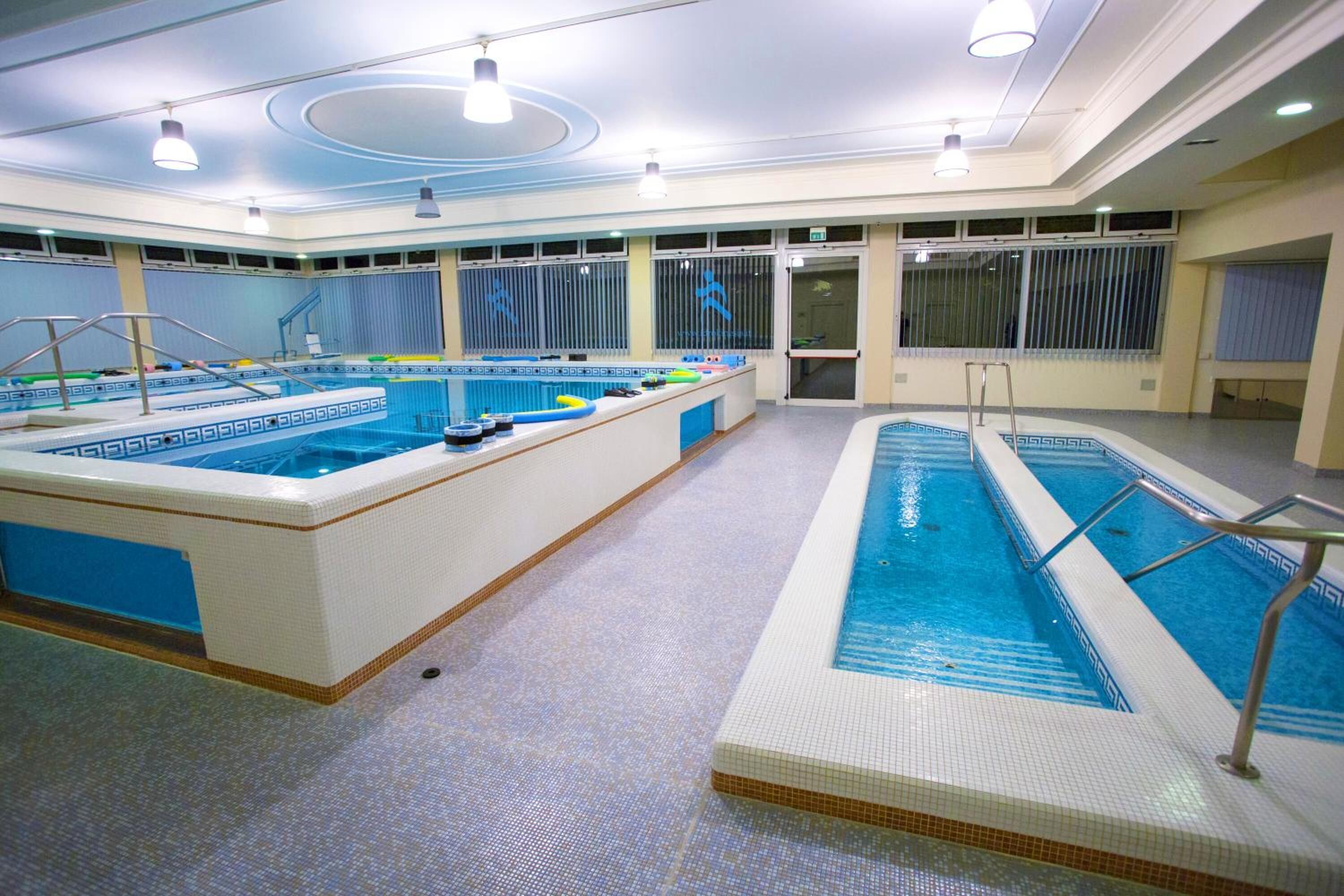 A large indoor swimming pool with multiple lanes, a changing room area, and a reception desk.