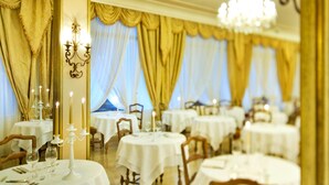 Une salle à manger élégante, avec des tables rondes, des nappes blanches et des rideaux dorés.