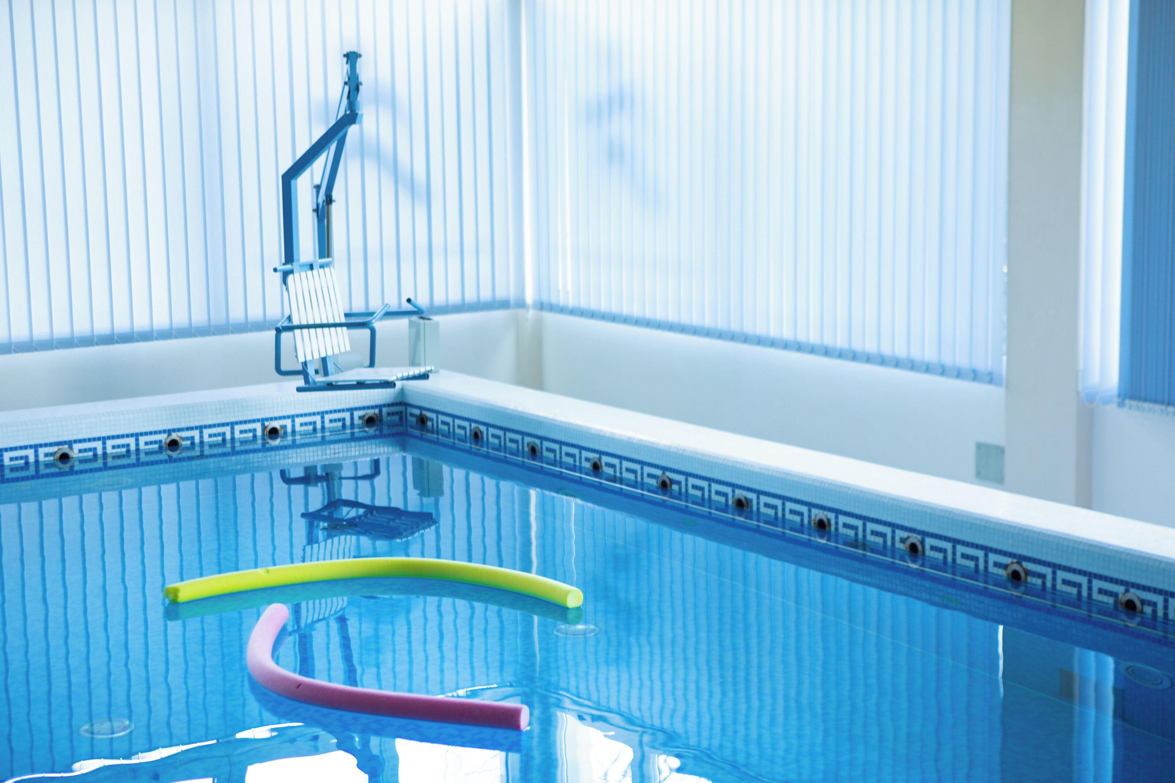 Une piscine à l’eau d’un bleu cristallin, avec un escalier et une zone aménagée au bord du bassin, une fenêtre visible au fond.