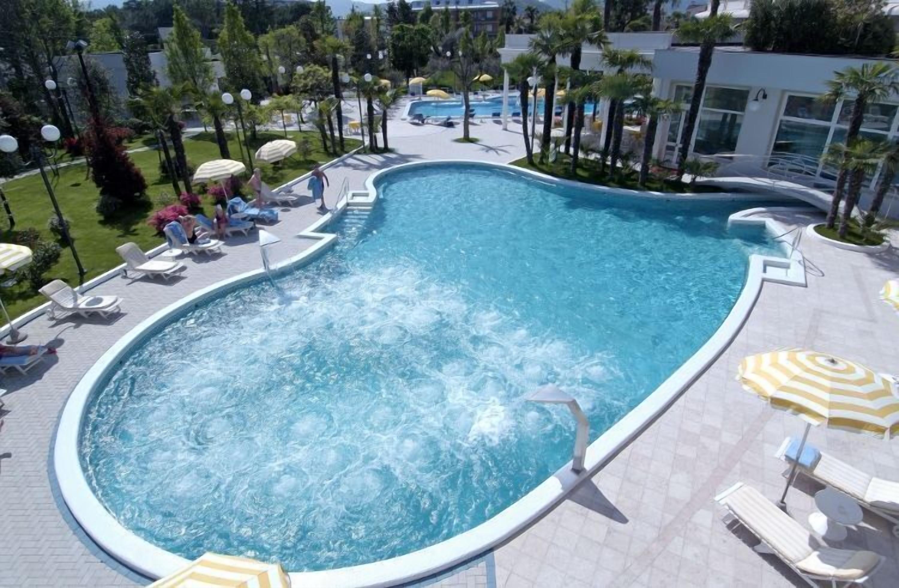 Una piscina amplia y de forma irregular, con numerosas tumbonas y sombrillas alrededor.